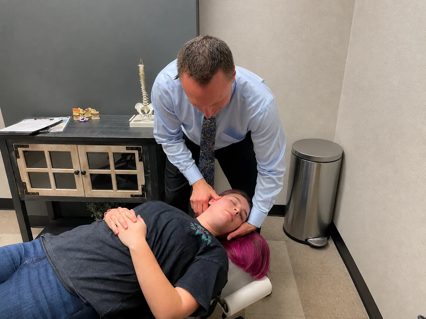 Dr. Charlie Gray adjusting the neck of a woman with pink-dyed hair lying face-up