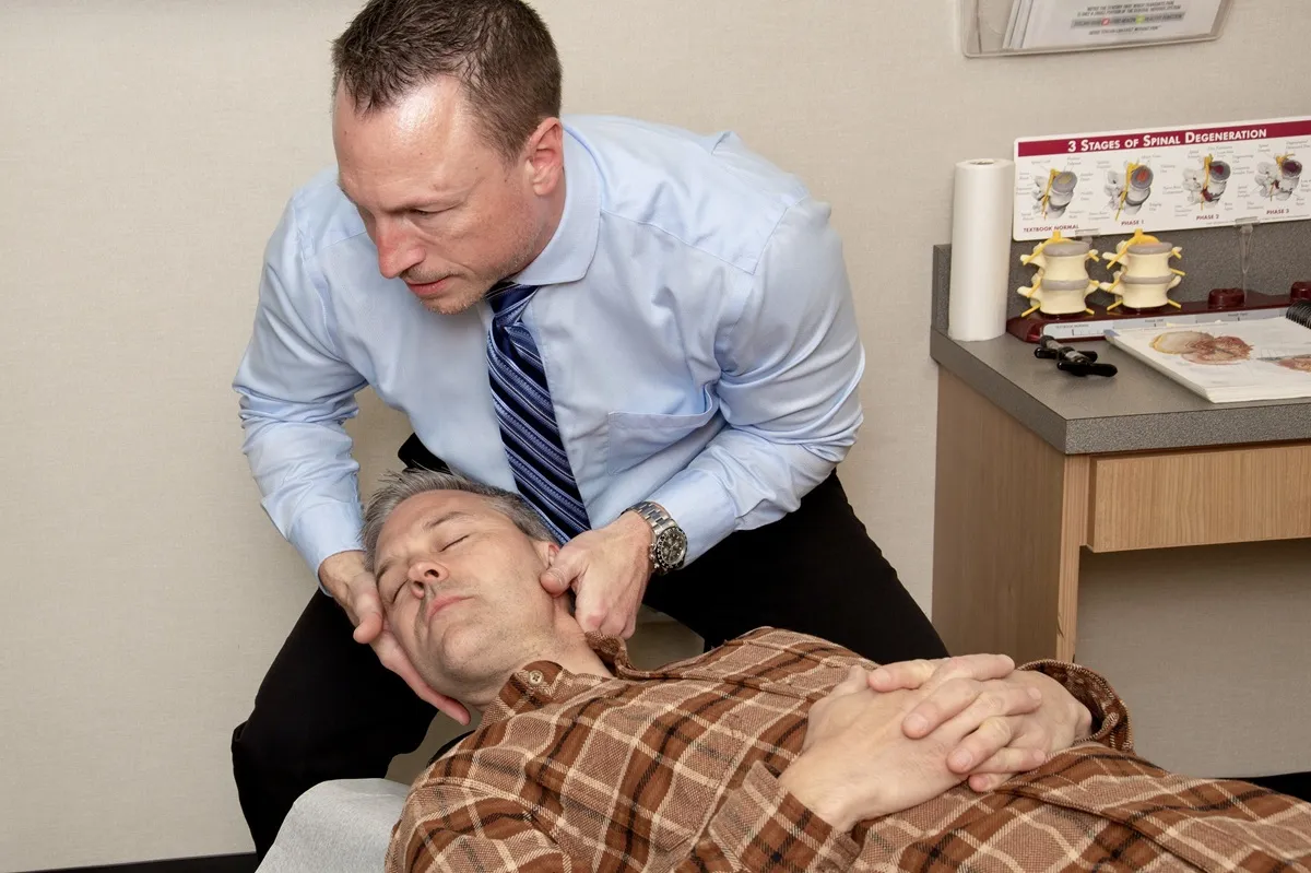 Dr. Charlie Gray cradling the head of a man in a plaid shirt to adjust his neck