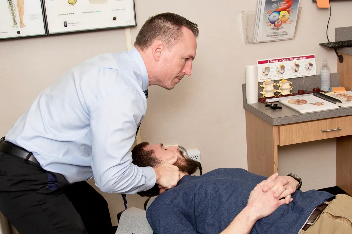 Dr. Charlie Gray adjusting the neck of a bearded man lying face-up