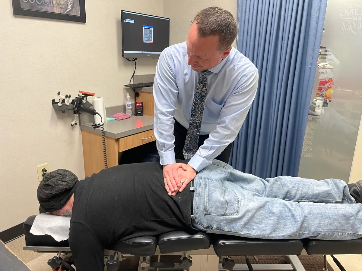 Dr. Charlie Gray pressing on the lower back of a man lying face-down on a chiropractic table