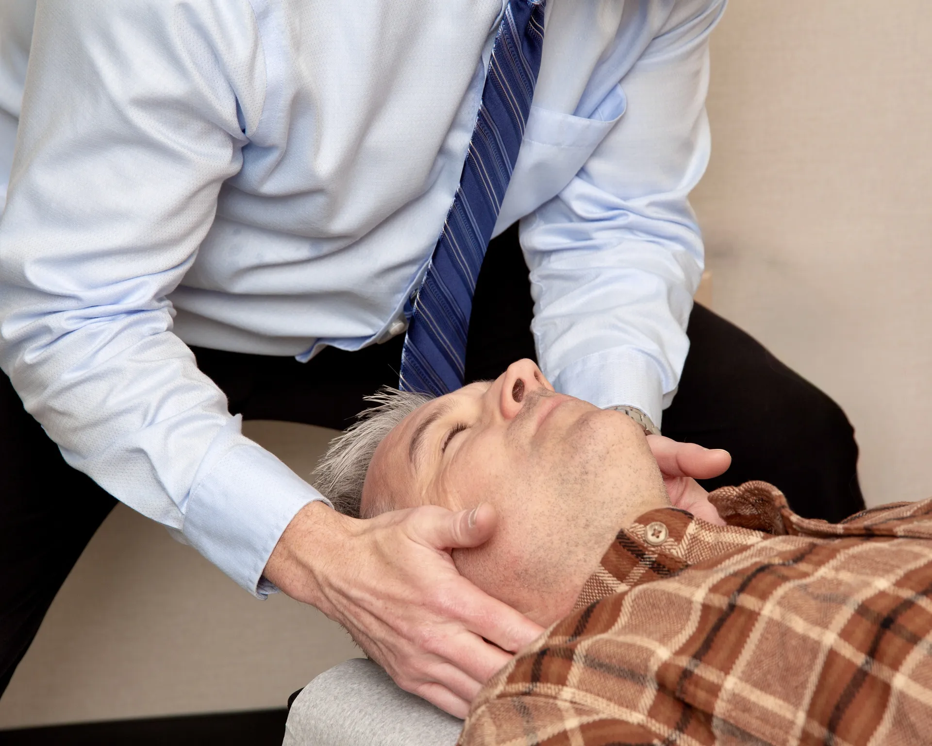 Close-up of a chiropractor's hands adjusting the neck of a man in a plaid shirt