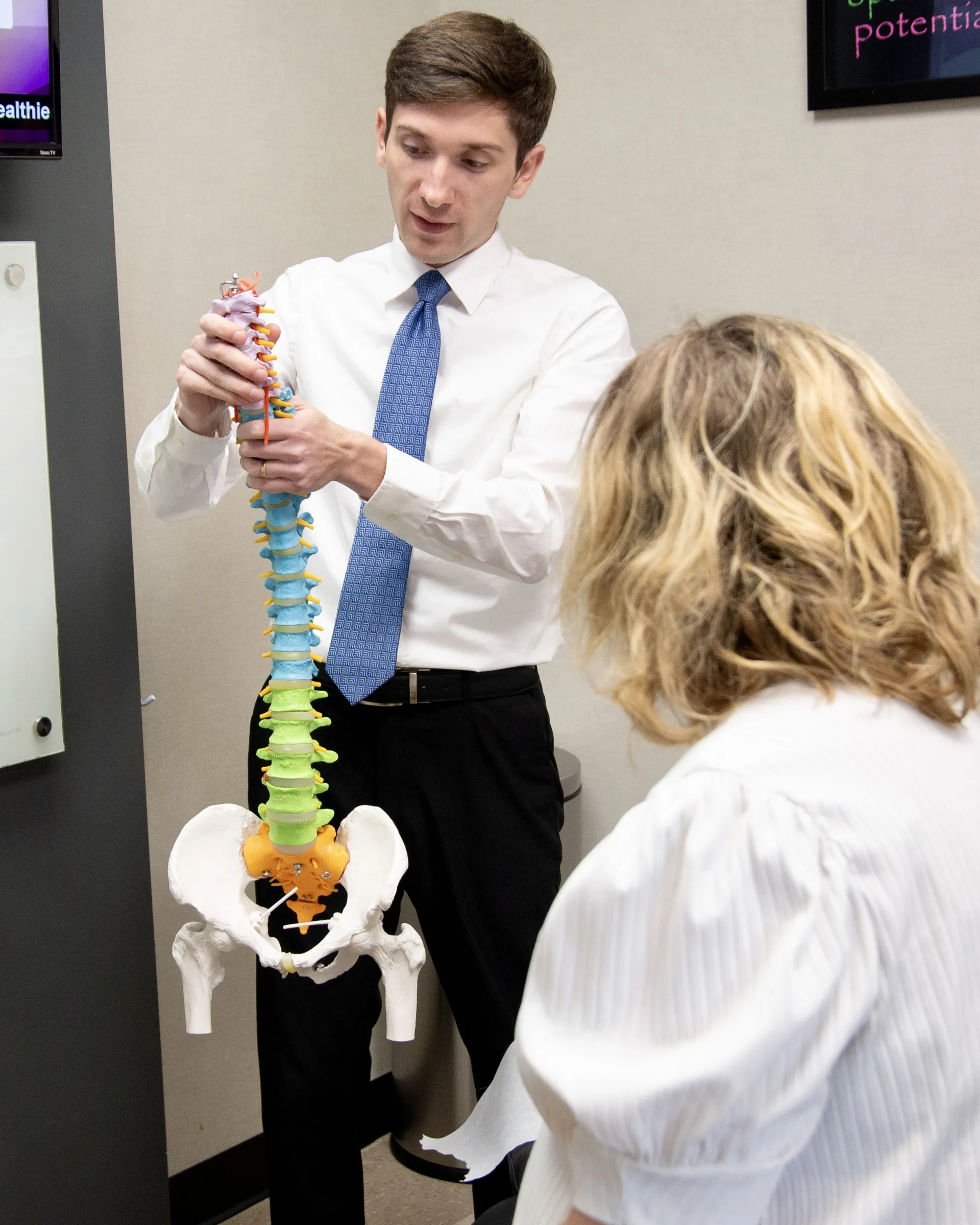 Chiropractor in a shirt and tie explaining a color-coded spine model to a patient