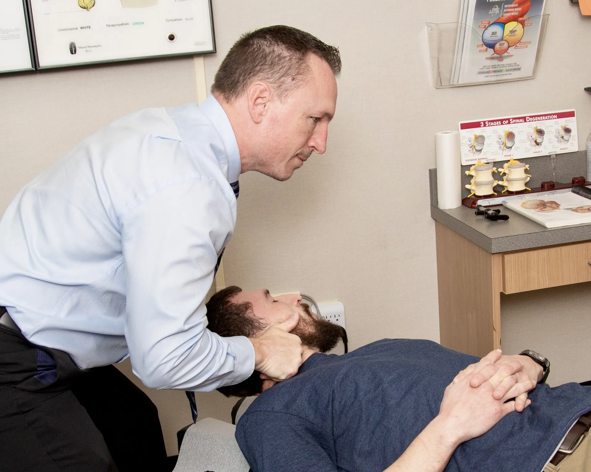 Dr. Charlie Gray adjusting the neck of a bearded man lying face-up on the table