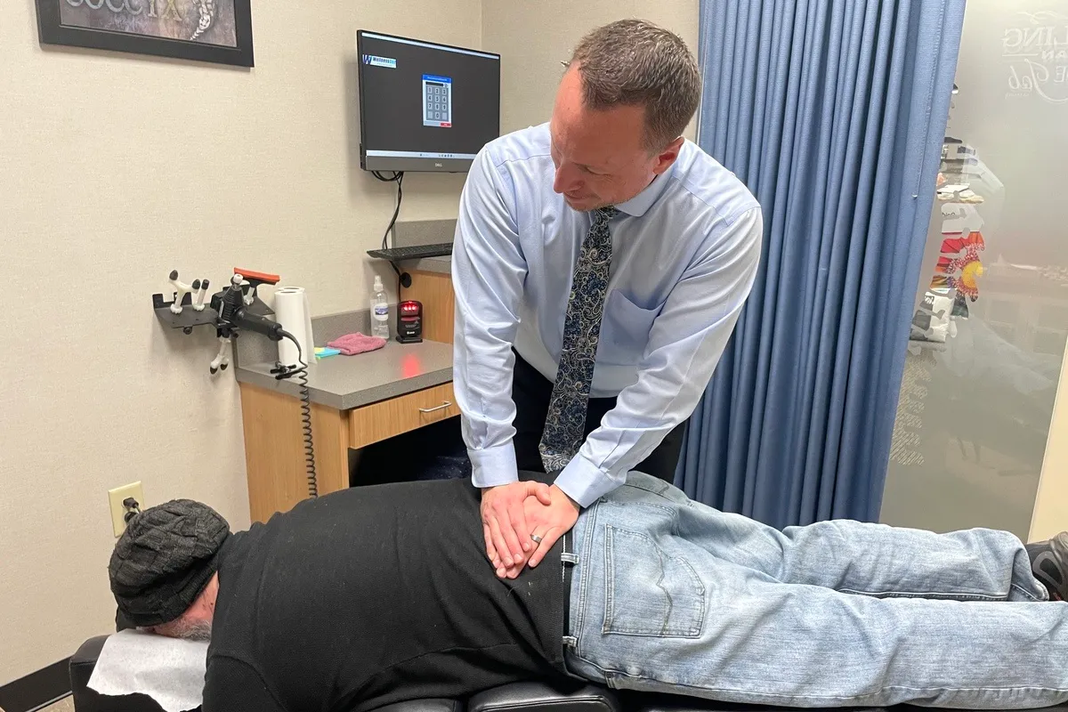 Dr. Charlie Gray adjusting the mid-back of a man in a beanie lying face-down