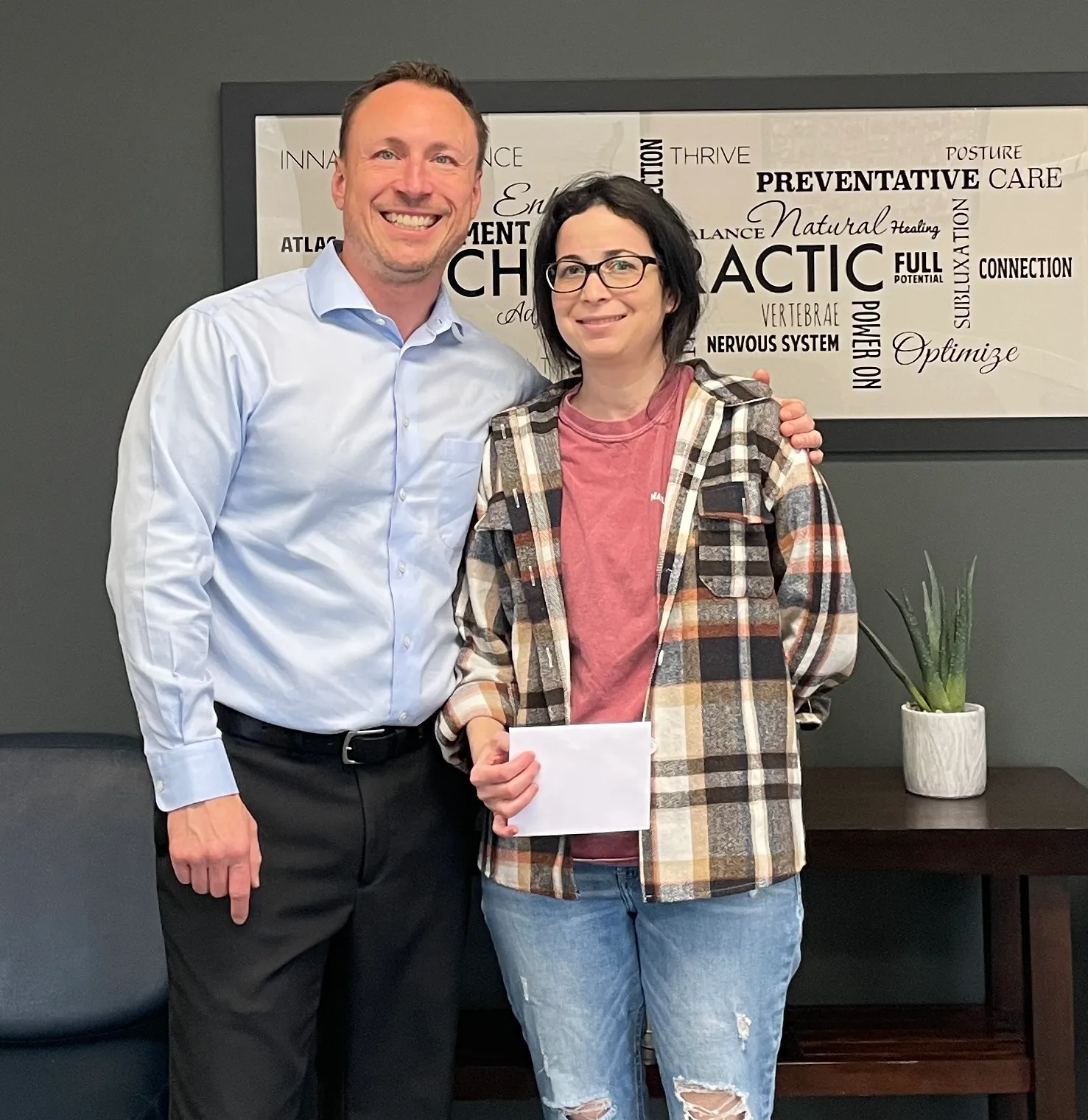 Chiropractor and a patient holding an envelope in front of chiropractic word art