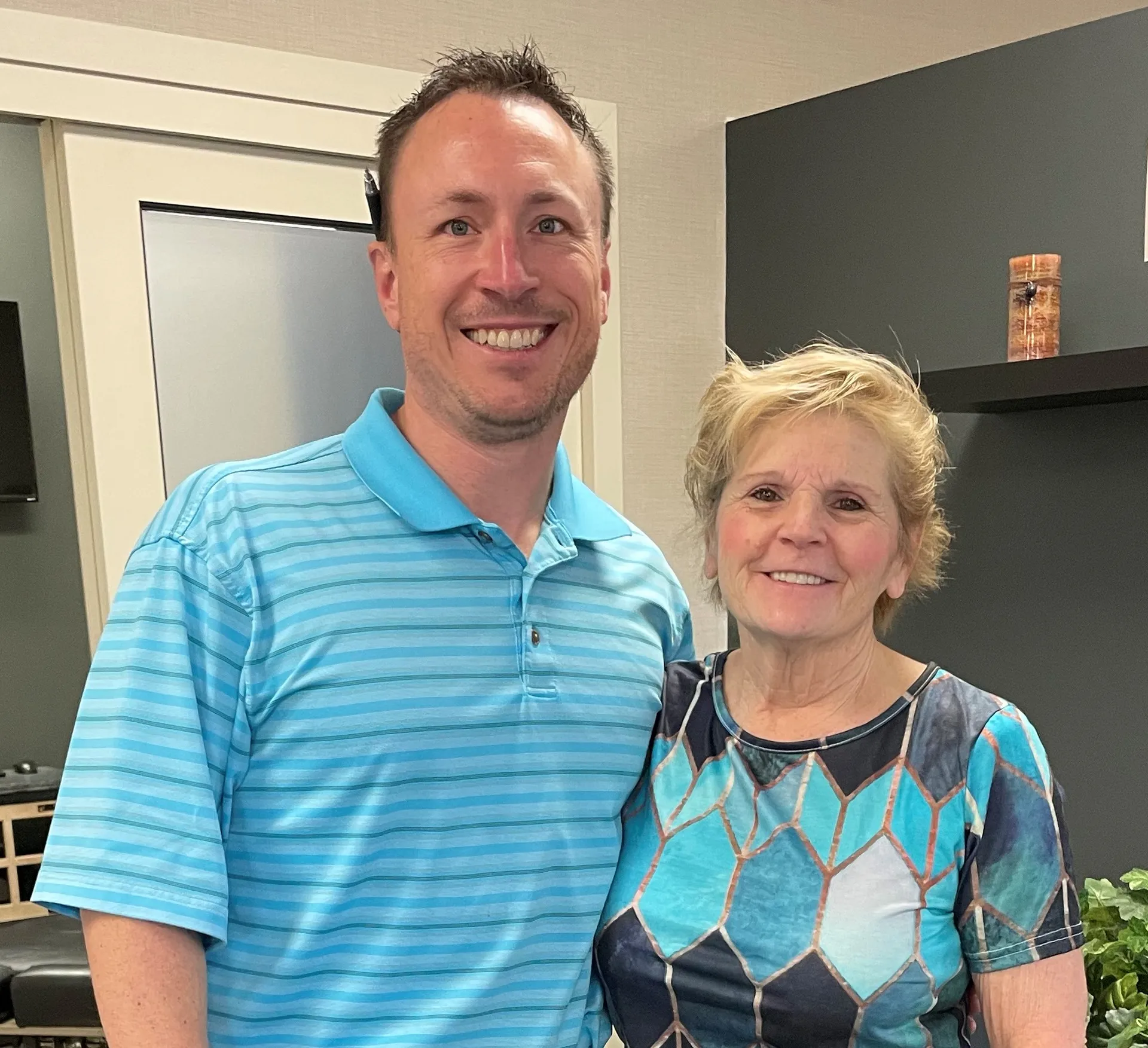 Chiropractor in a blue striped polo standing with a smiling patient in the clinic