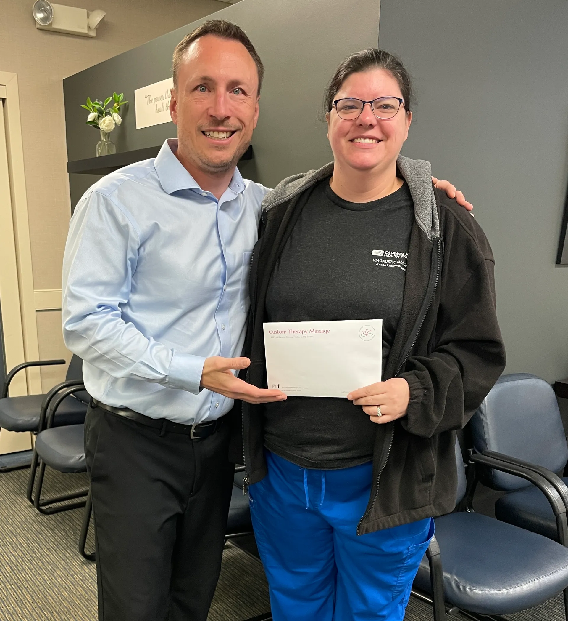 Chiropractor in a blue dress shirt with a smiling patient holding an envelope
