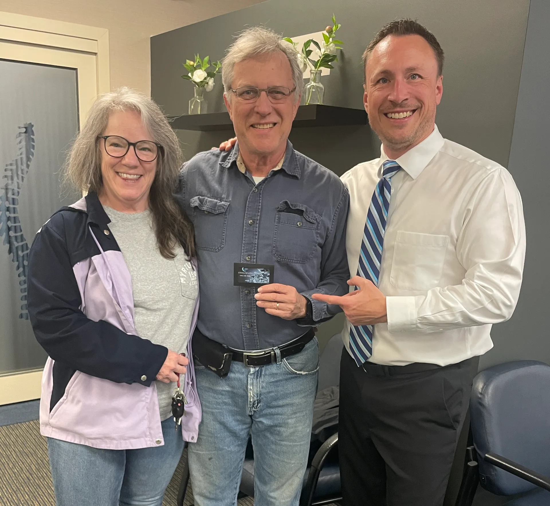 Dr. Charlie Gray with a smiling couple, one holding a card, in the clinic