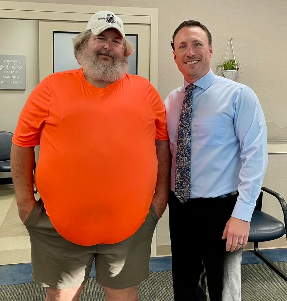 Dr. Charlie Gray with a bearded patient in an orange T-shirt and cap