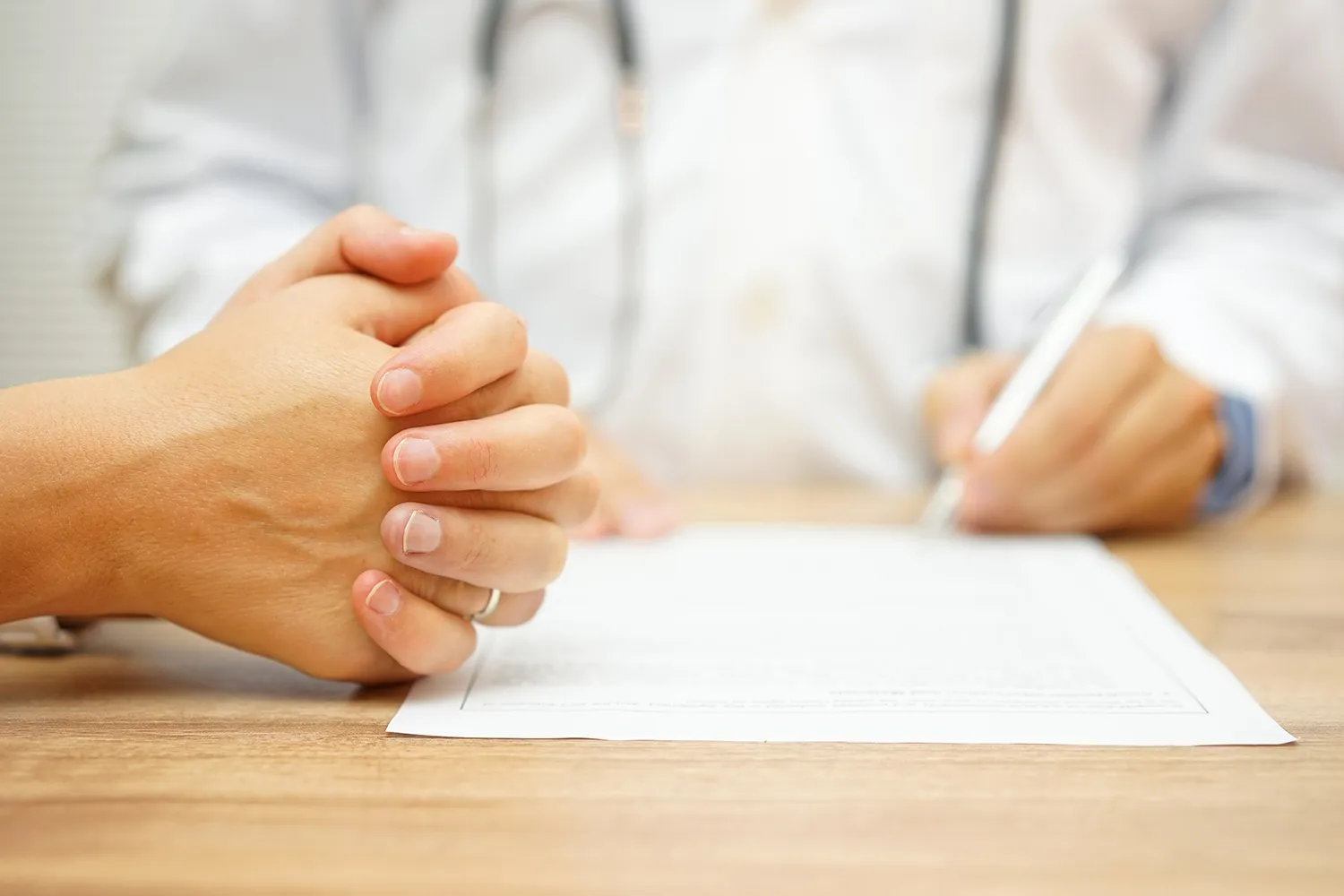 Doctor writing notes on a report across the desk from a patient