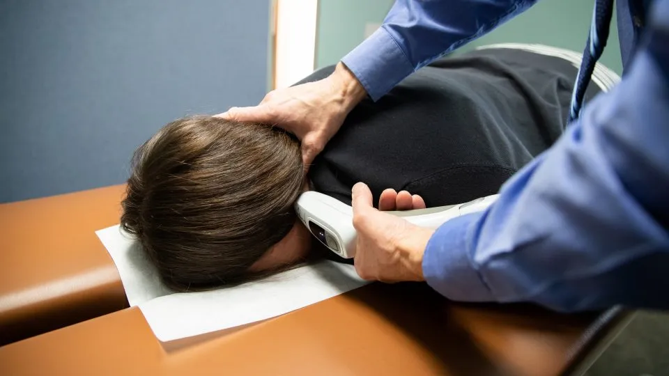 Chiropractor using an Activator instrument at the base of a face-down patient's skull