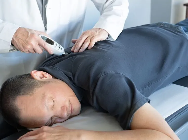 Chiropractor using an Activator instrument on the upper back of a man lying face-down