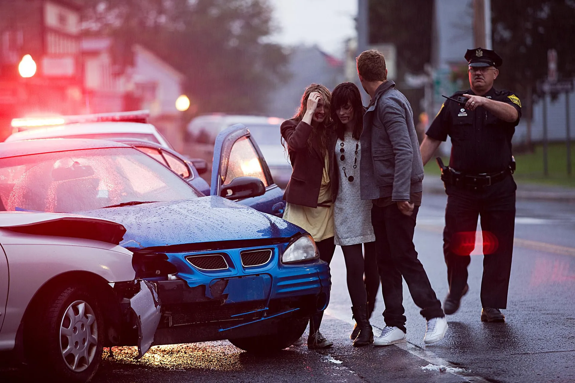 Shaken people and a police officer beside a damaged car at a crash scene