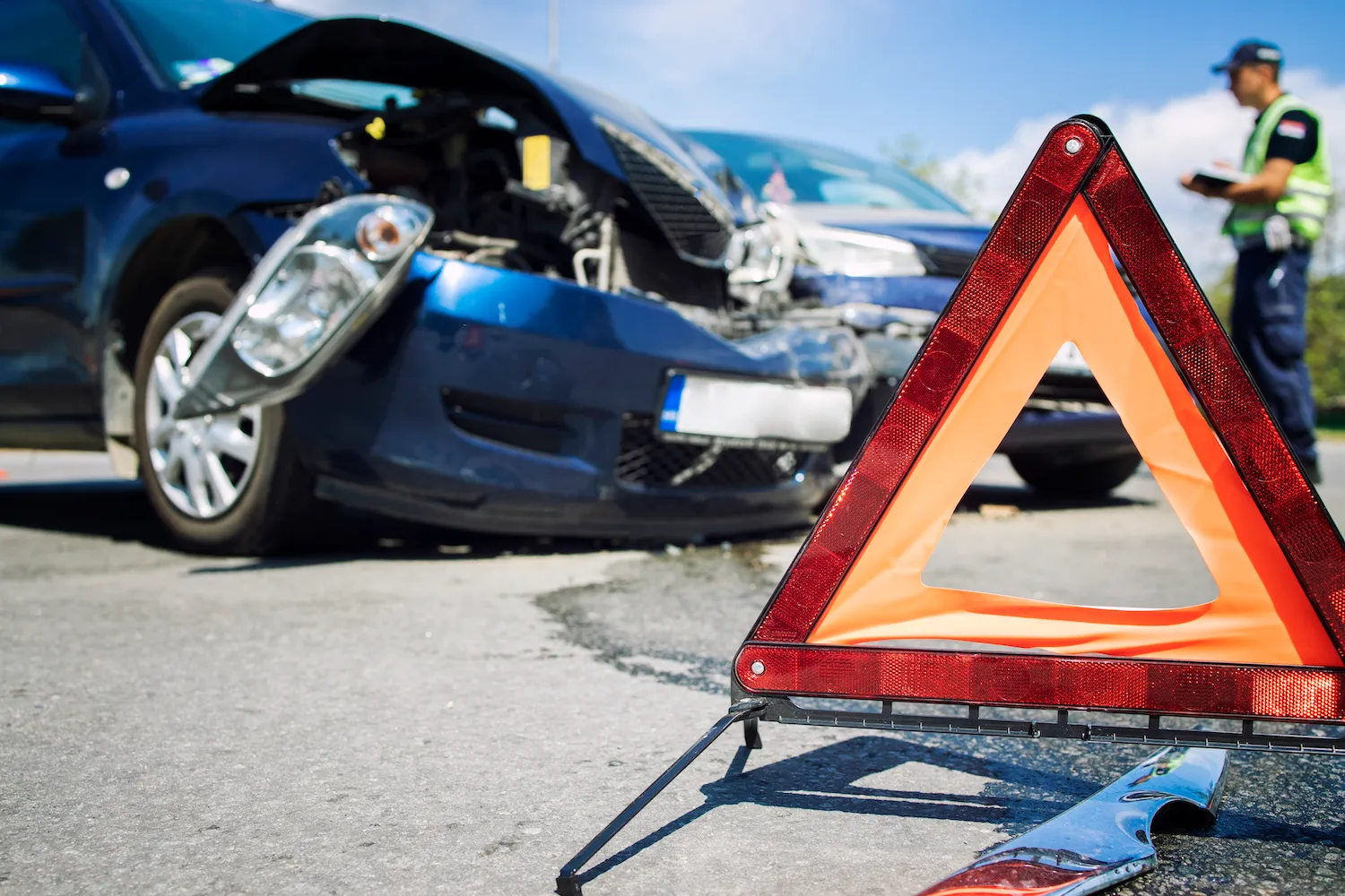Red warning triangle on the road in front of a crashed blue car