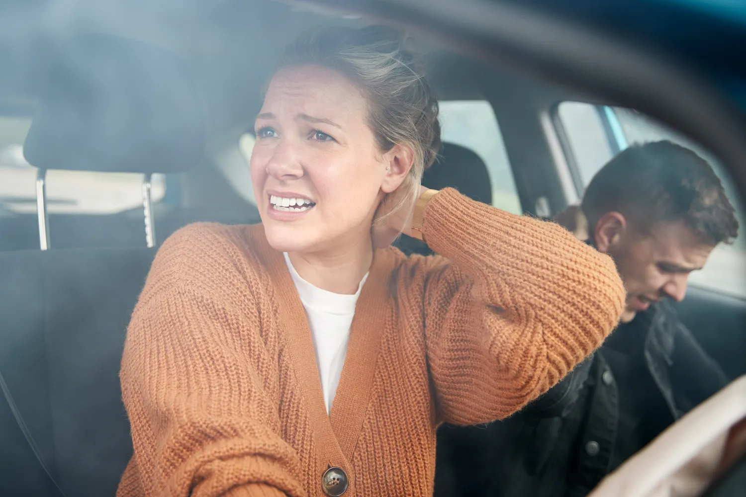 Woman in a car holding her neck in pain after an accident, with a man slumped beside her