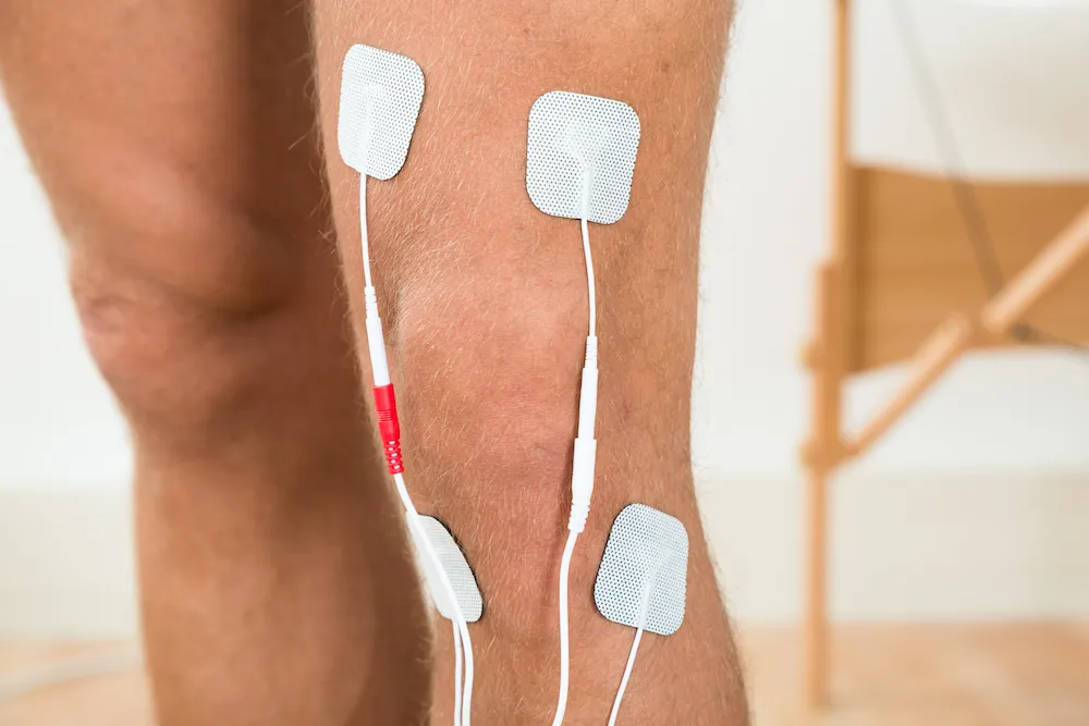 Four electrotherapy electrode pads on the back of a person's leg around the knee