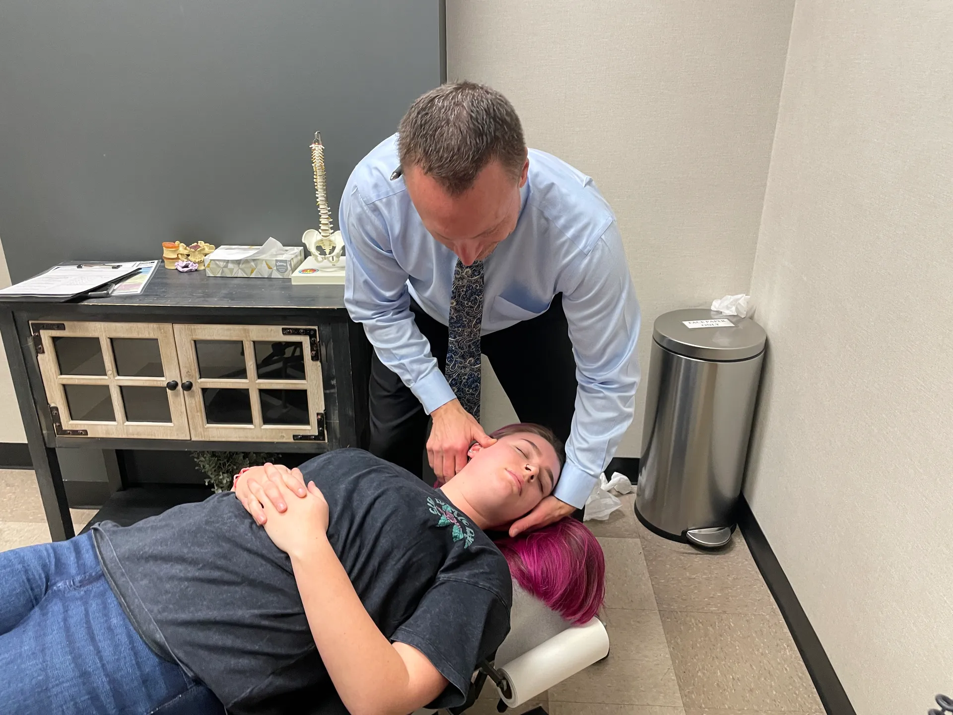 Dr. Charlie Gray adjusting the neck of a young woman lying face-up on the table