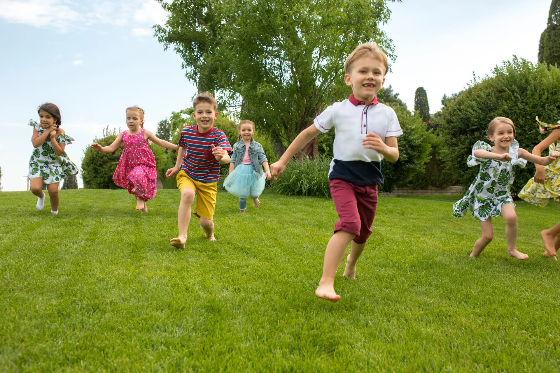 Group of young children running barefoot across a lawn