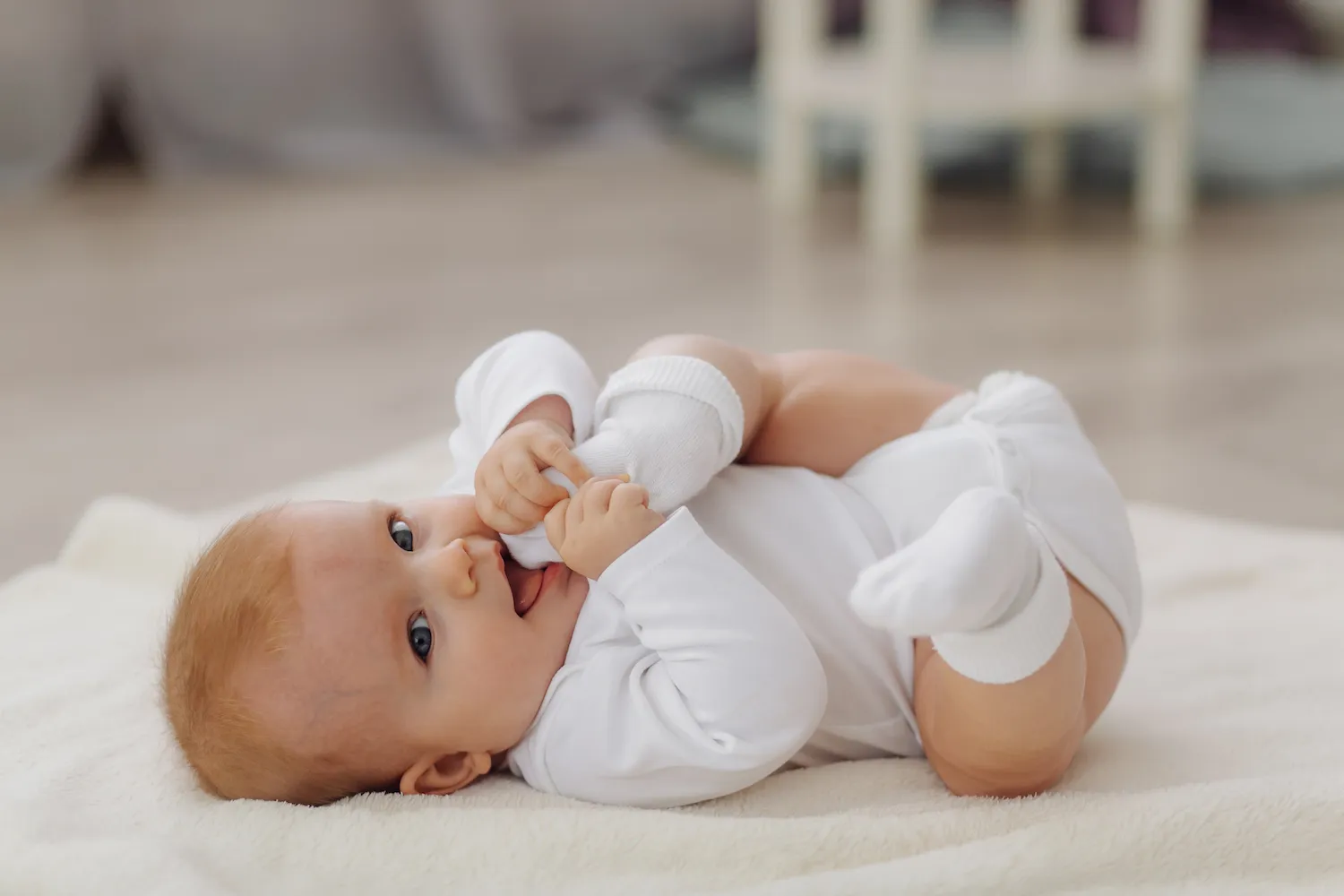 Smiling baby in a white onesie lying on a soft blanket