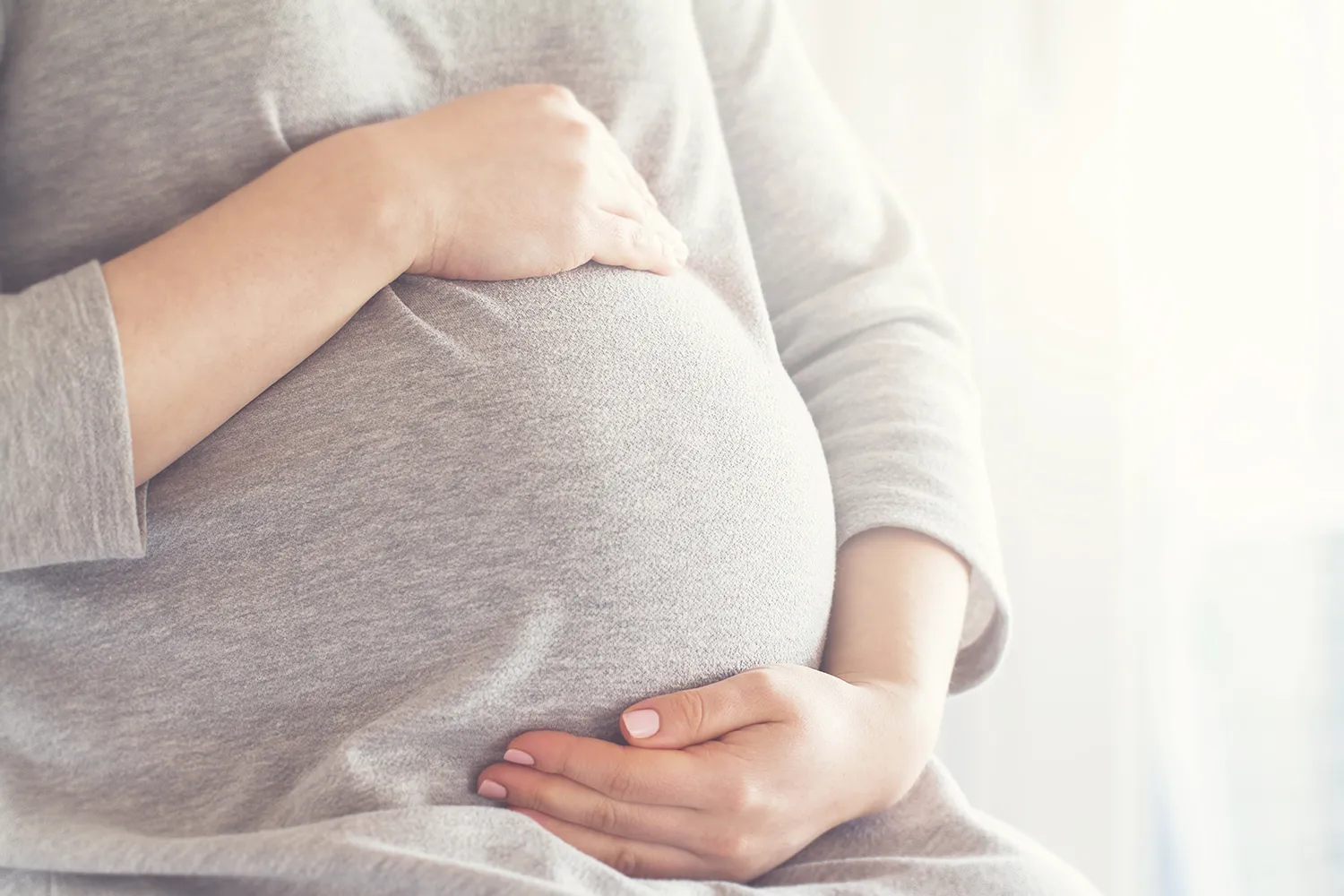 Close-up of a pregnant woman cradling her belly with both hands