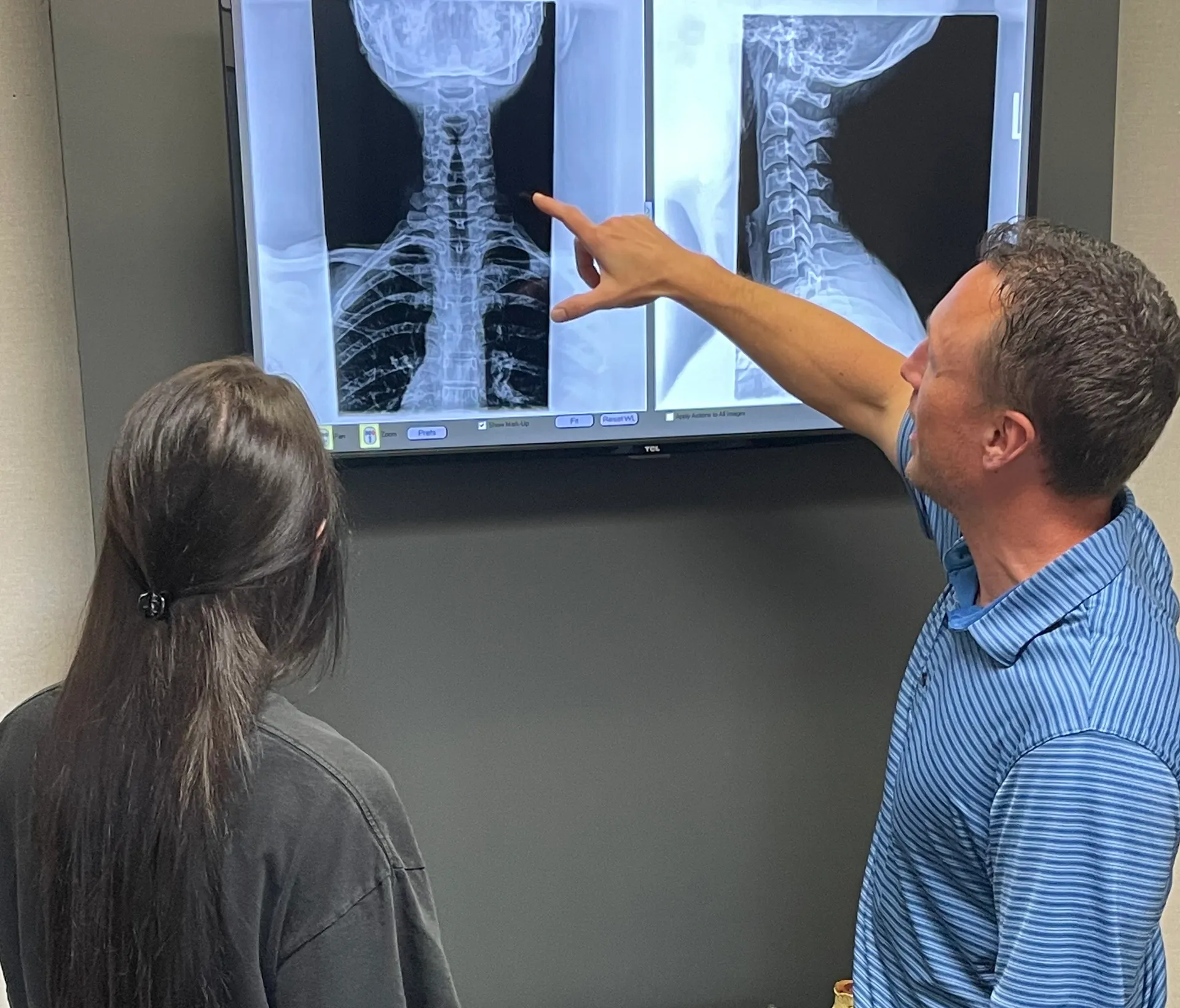 Chiropractor pointing out details on spine X-rays on a wall monitor for a patient