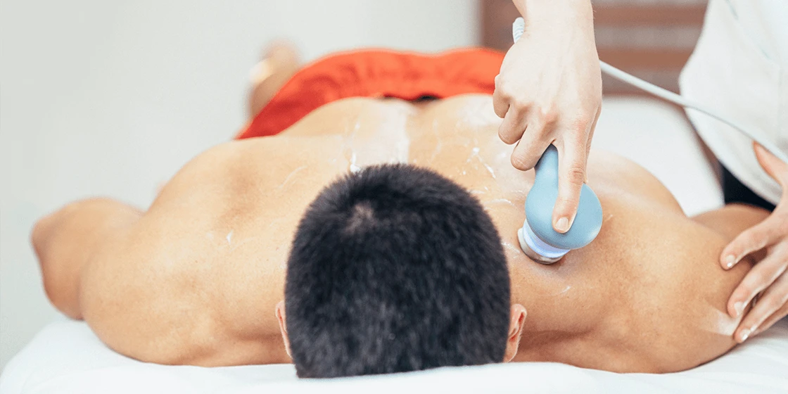 Therapist moving an ultrasound probe over the upper back of a man lying face-down