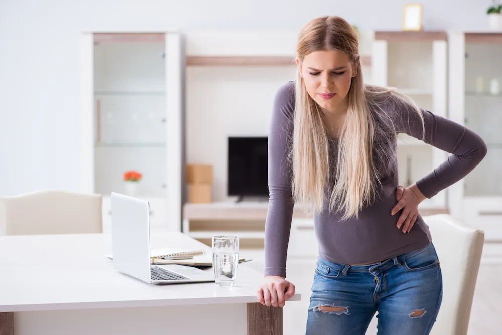 Woman leaning on a table and holding her lower back in pain