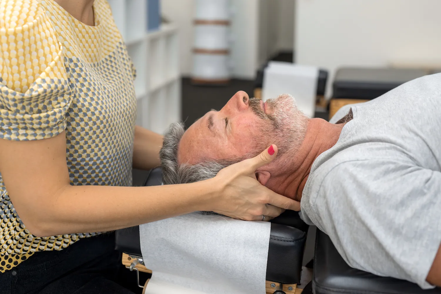 Practitioner cradling a man's head and neck as he lies face-up on a treatment table
