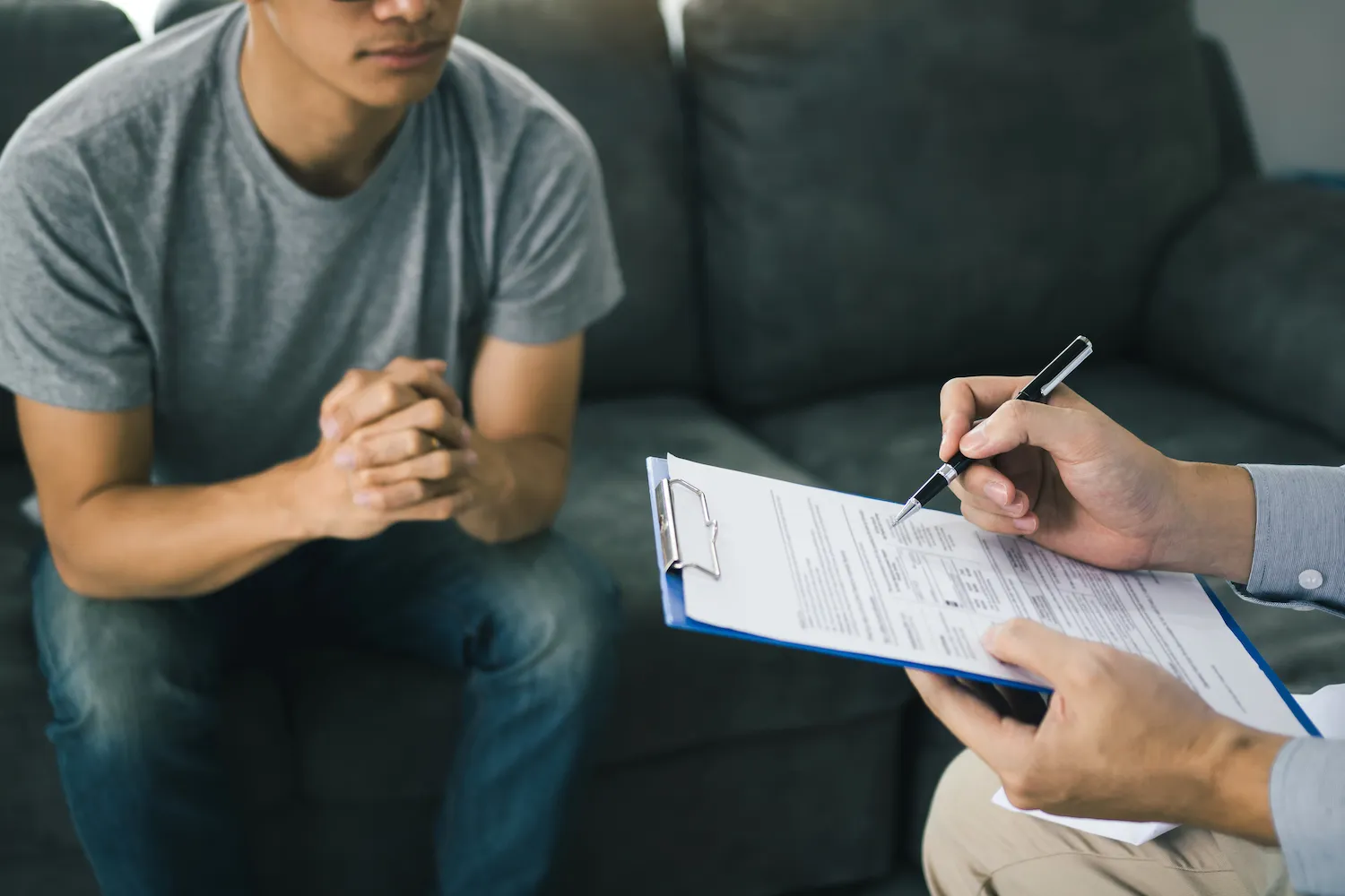 Young man on a couch while a practitioner fills in an intake form on a clipboard