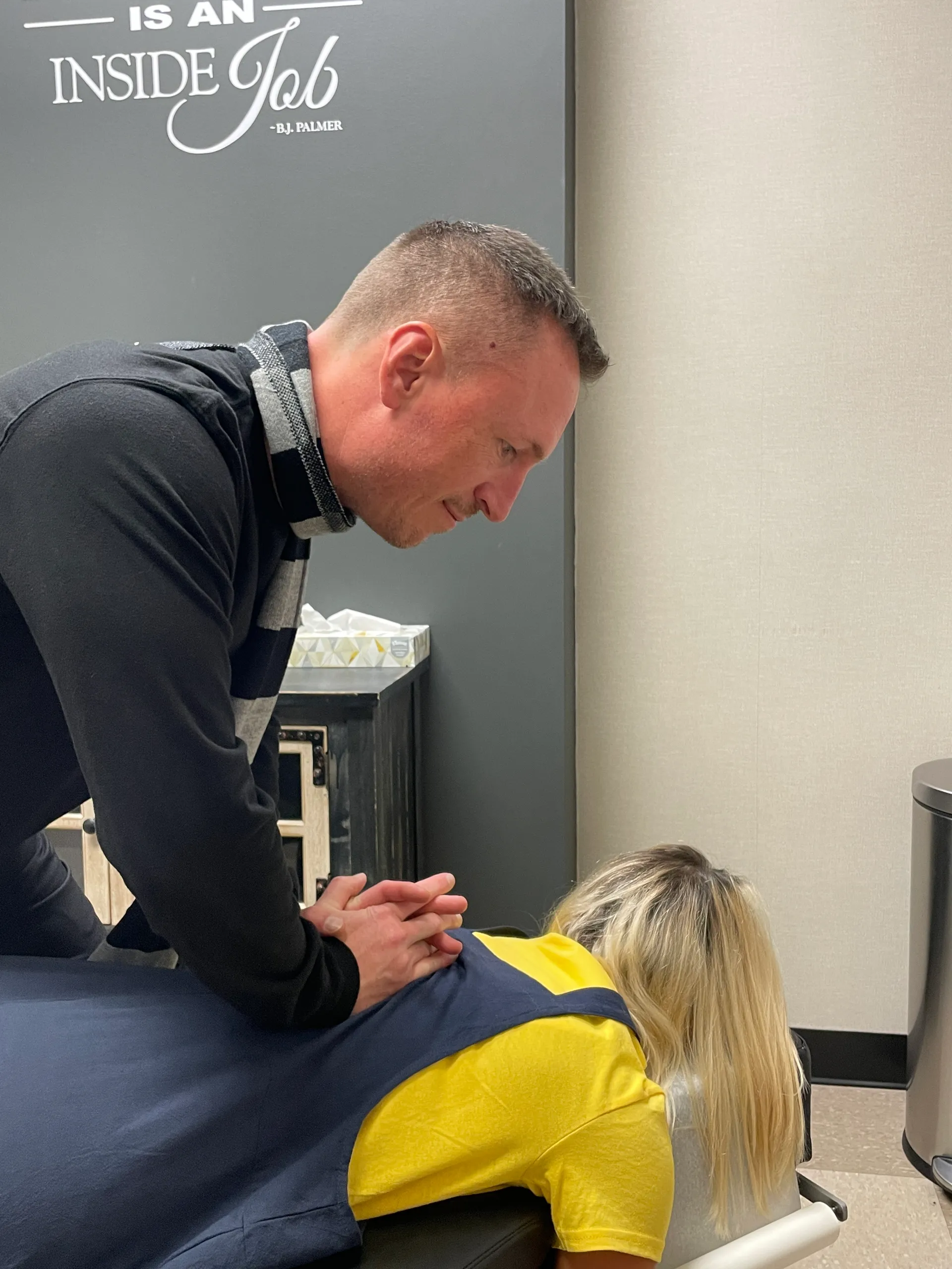 Chiropractor in a dark sweater adjusting the upper back of a woman lying face-down