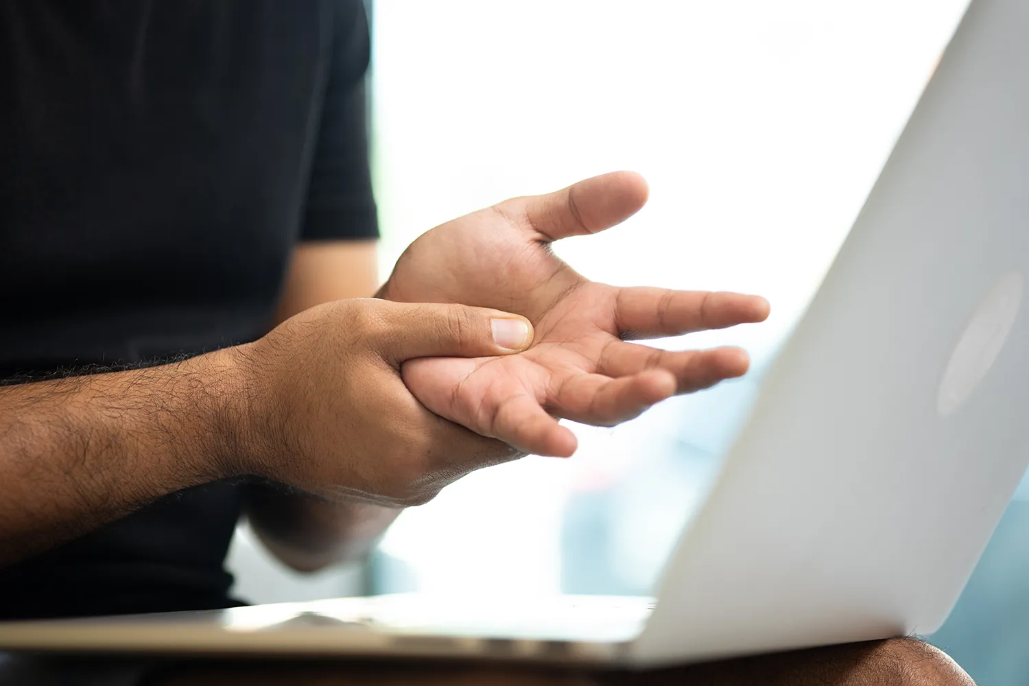 Man at a laptop rubbing the palm of his hand