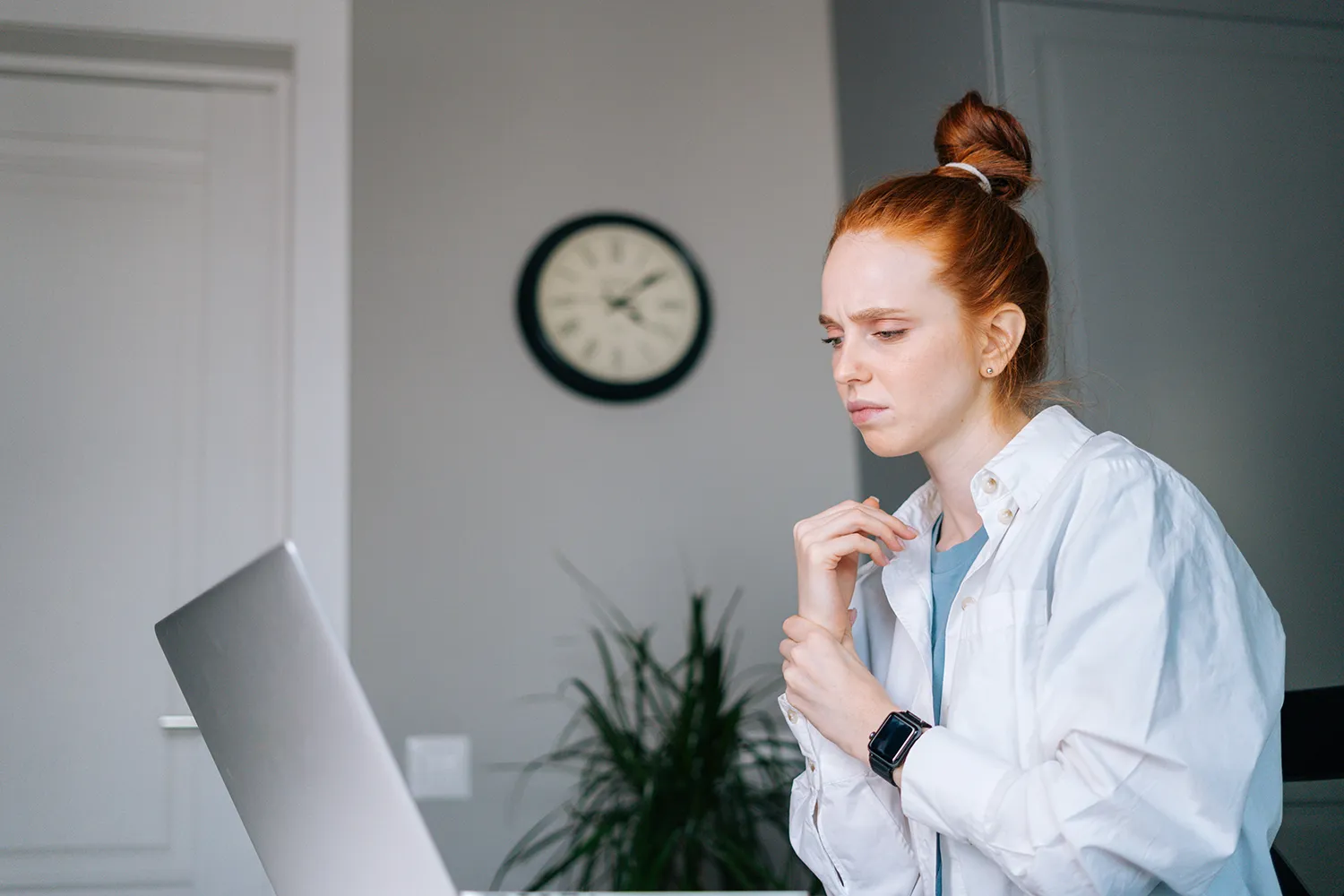 Red-haired woman at a laptop wincing as she rubs her wrist