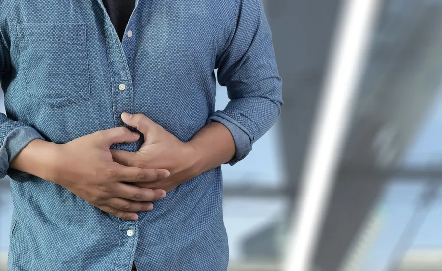 Man in a denim shirt holding his stomach in discomfort