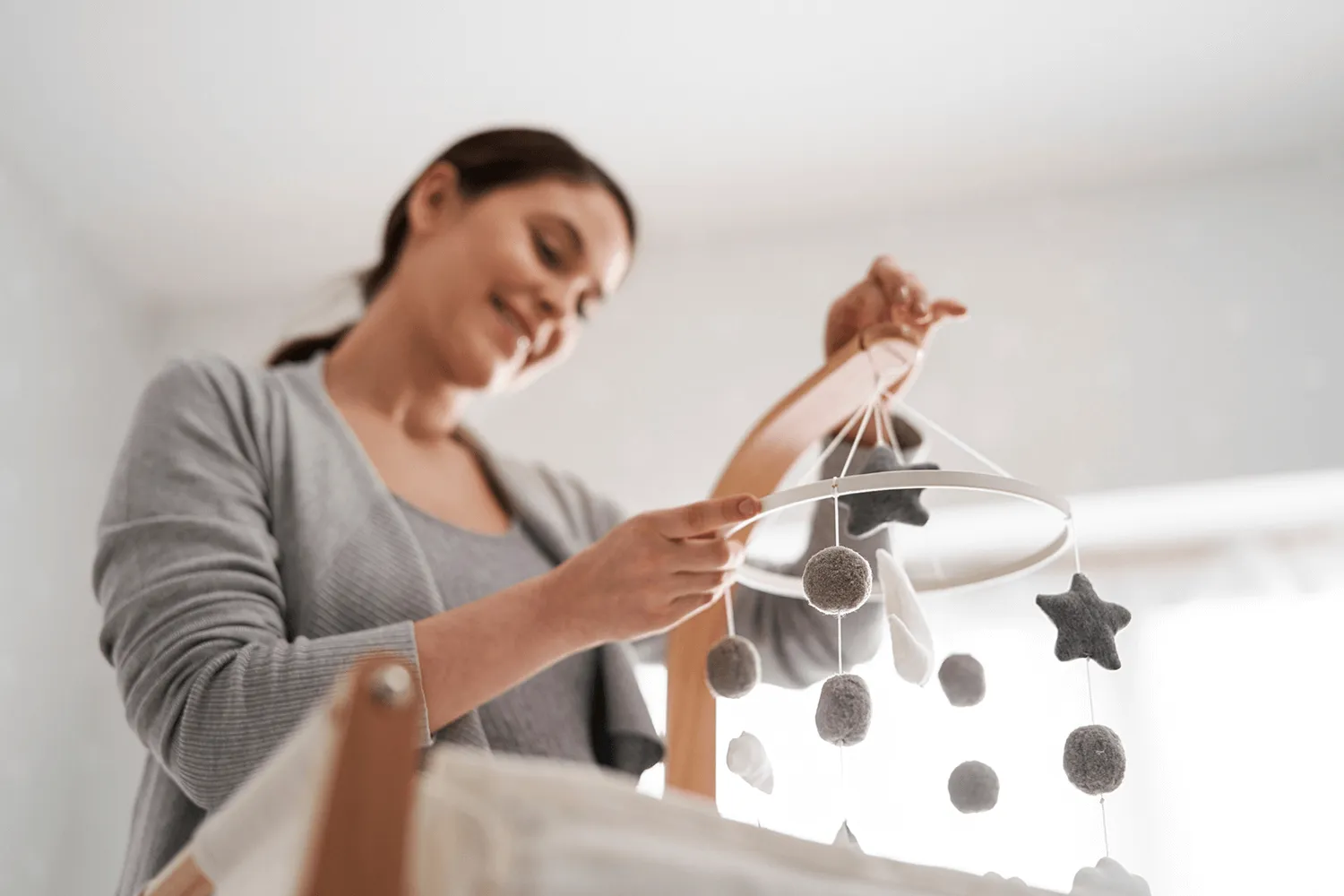 Smiling woman hanging a mobile above a baby crib
