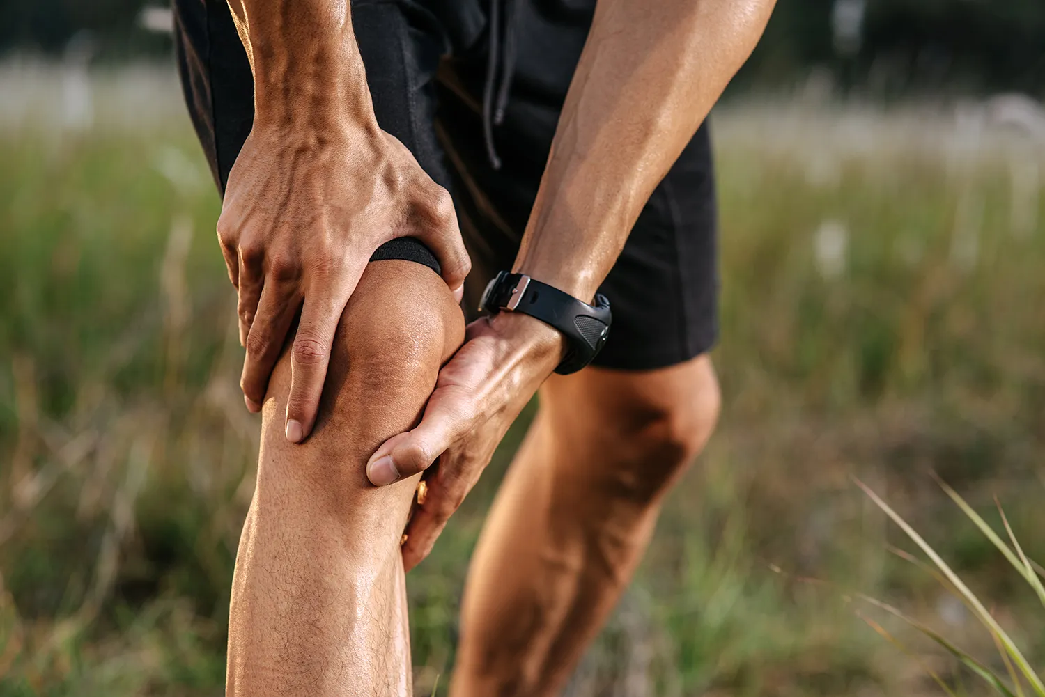 Close-up of a runner gripping a sore knee outdoors