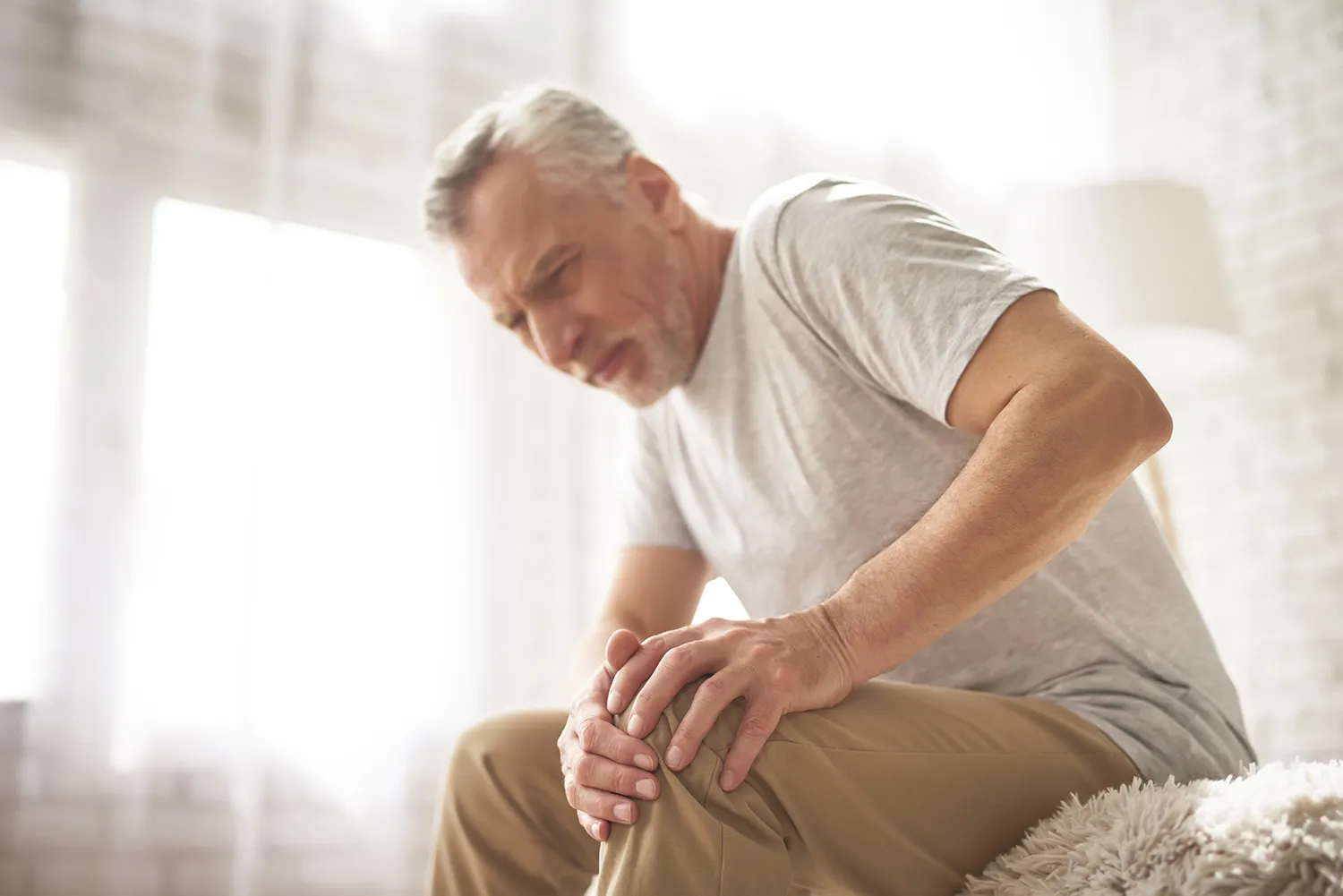 Older man sitting on a bed holding his painful knee