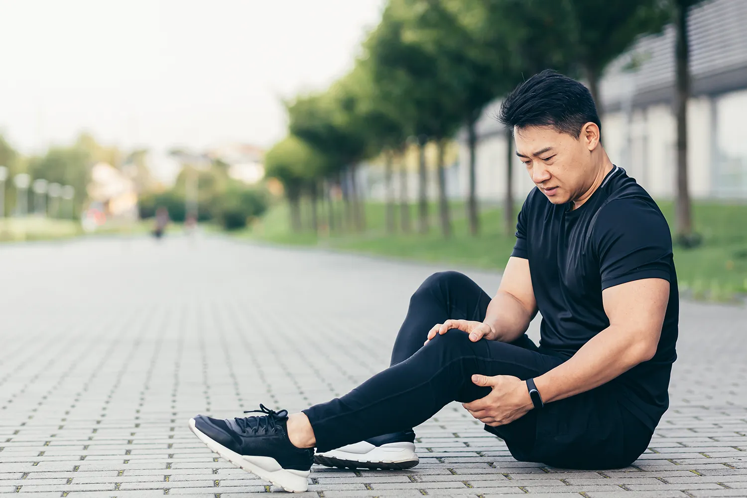 Man in workout clothes sitting on the pavement holding his knee