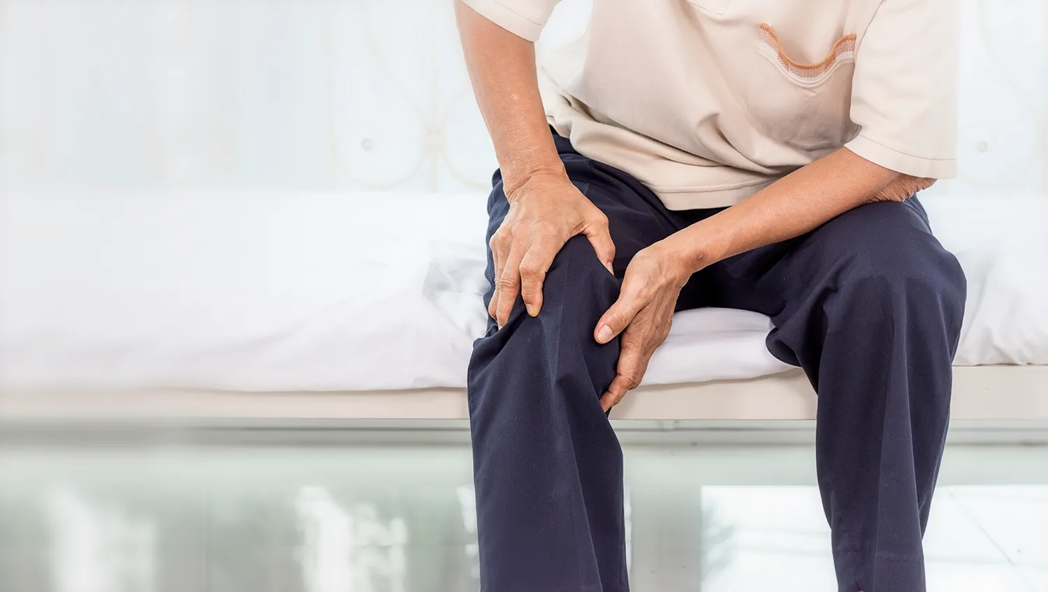 Person sitting on the edge of a bed gripping both legs above the knees