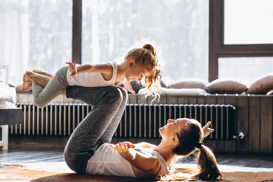 Mother balancing her daughter on her feet during playful yoga at home