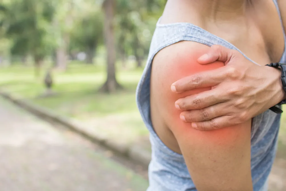 Person outdoors holding a shoulder highlighted red with pain