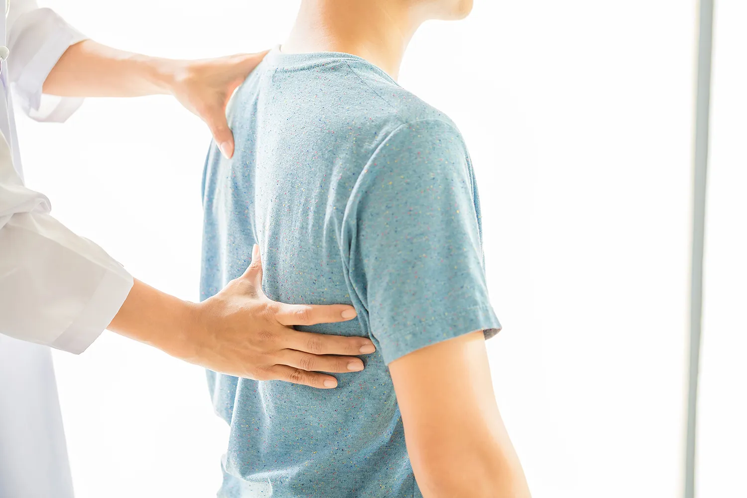 Practitioner placing hands on a young person's back and shoulder to check posture