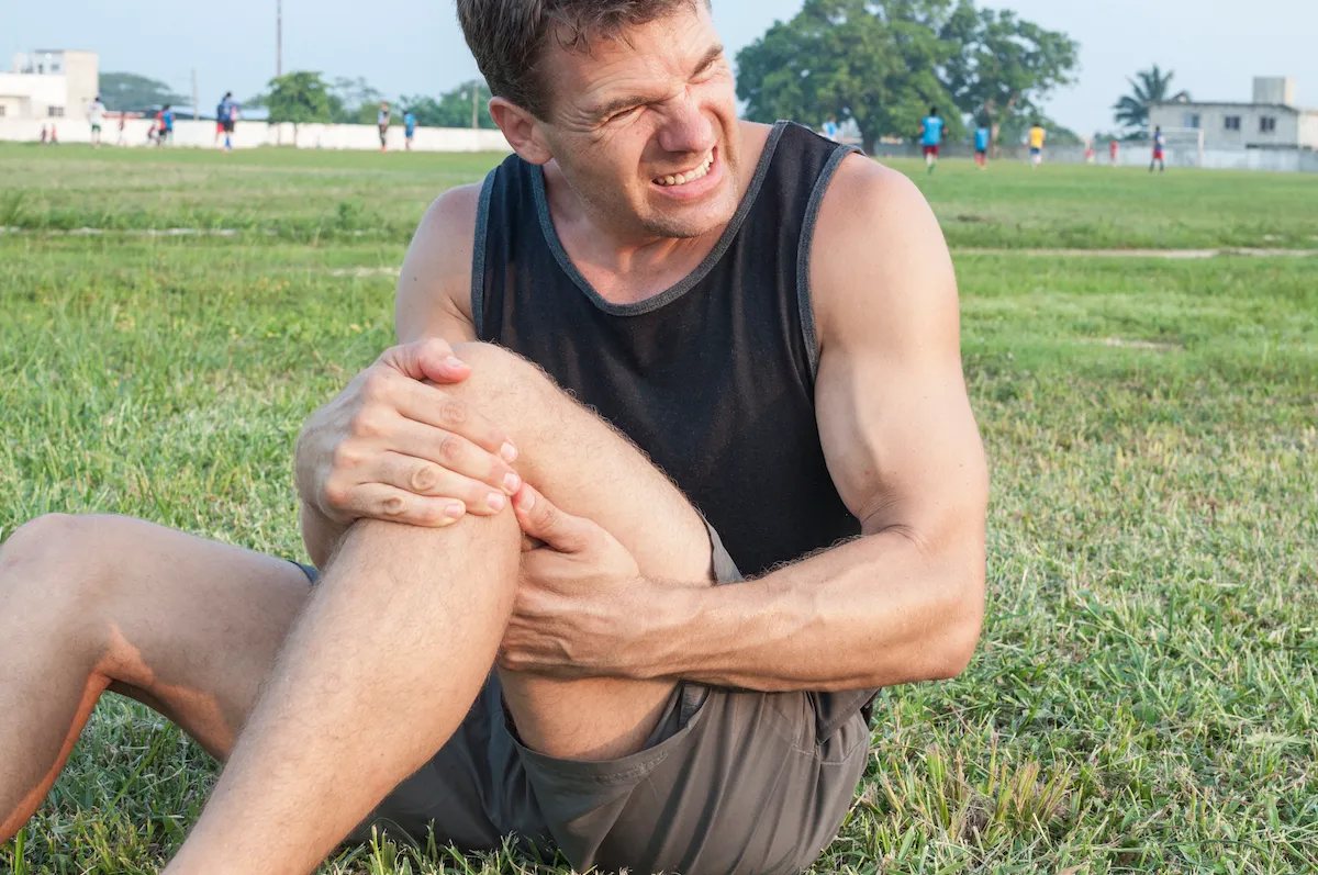 Man sitting on grass grimacing and clutching his knee