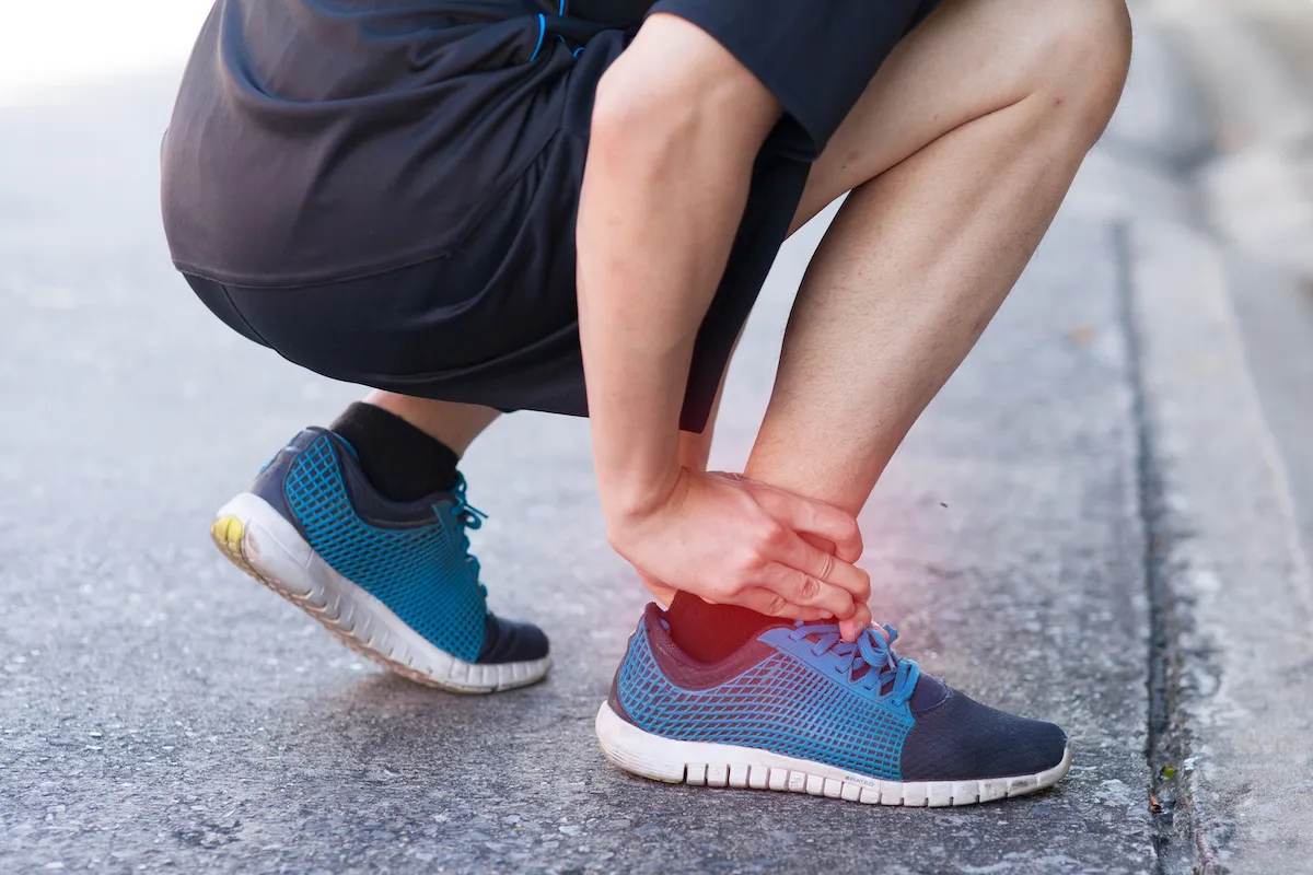 Runner crouching on the road holding a red, painful ankle