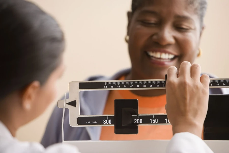 Smiling woman having her weight checked on a medical scale by a clinician