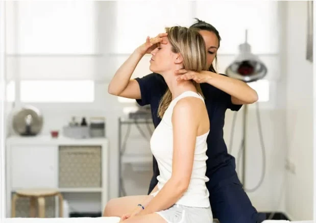 Practitioner working on the neck of a seated woman in a bright treatment room