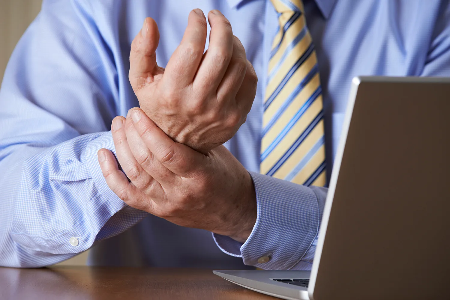 old man having a wrist pain while working on his laptop