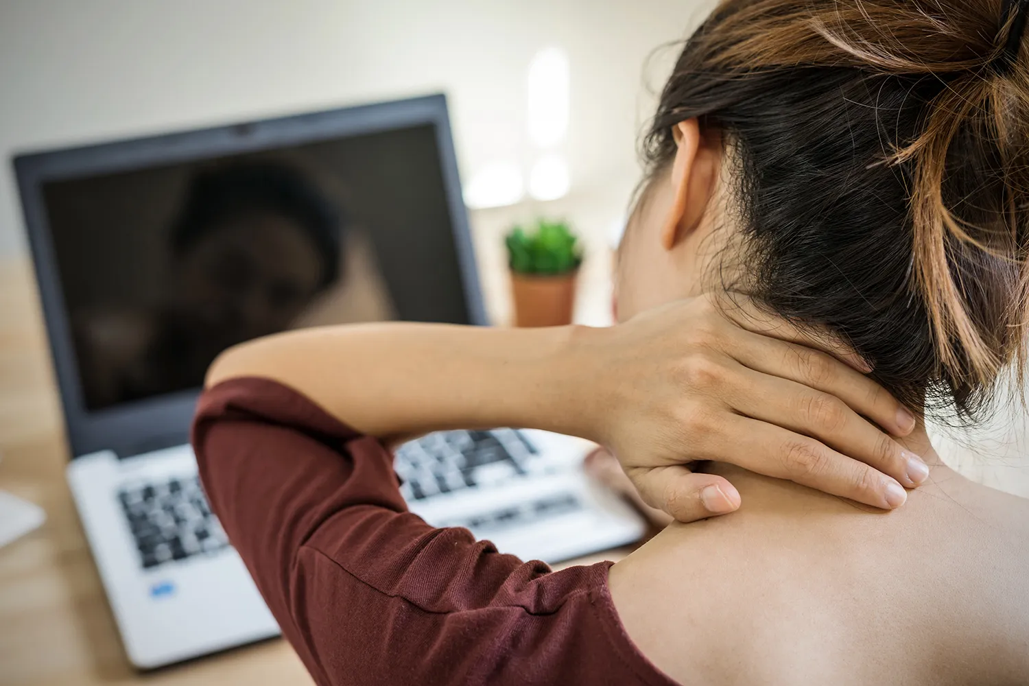 Woman at a laptop rubbing the back of her neck